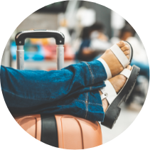 Lioton® Gel în călătorie, o persoană stă pe o bancă cu picioarele sprijinite deasupra unui rucsac.